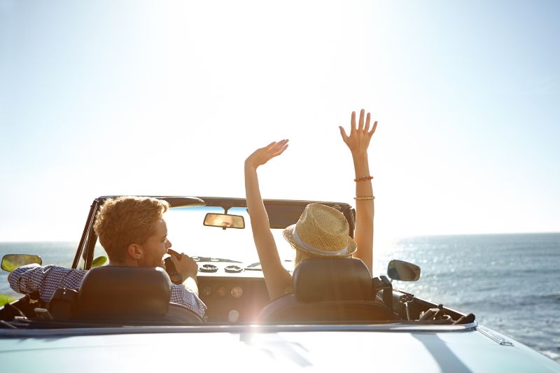 Una pareja joven disfruta de su coche descapotable en un paisaje soleado y marítimo.