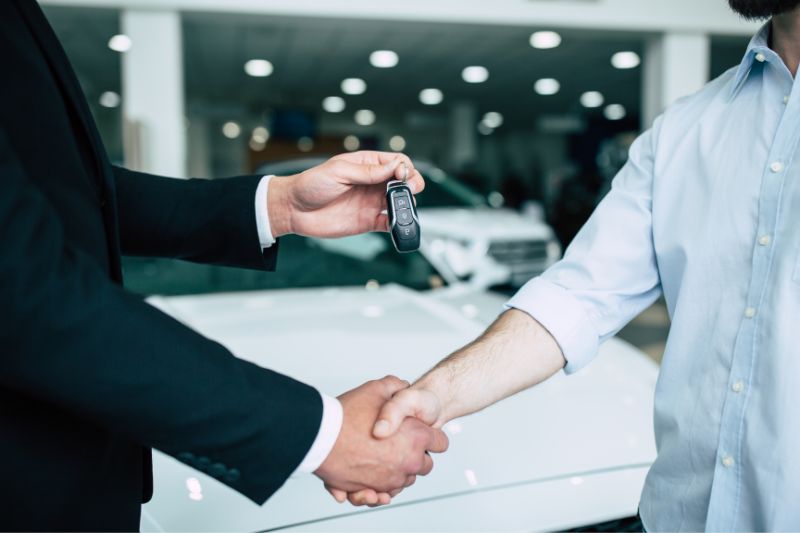 Un comercial entrega las llaves del coche nuevo a un comprador en el concesionario y estrechan las manos.