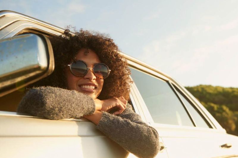 Chica saca la cabeza por la ventanilla de un coche y sonríe