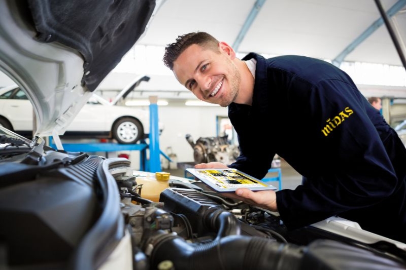 Un mecánico de Midas sonrie a cámara mientras repara un coche